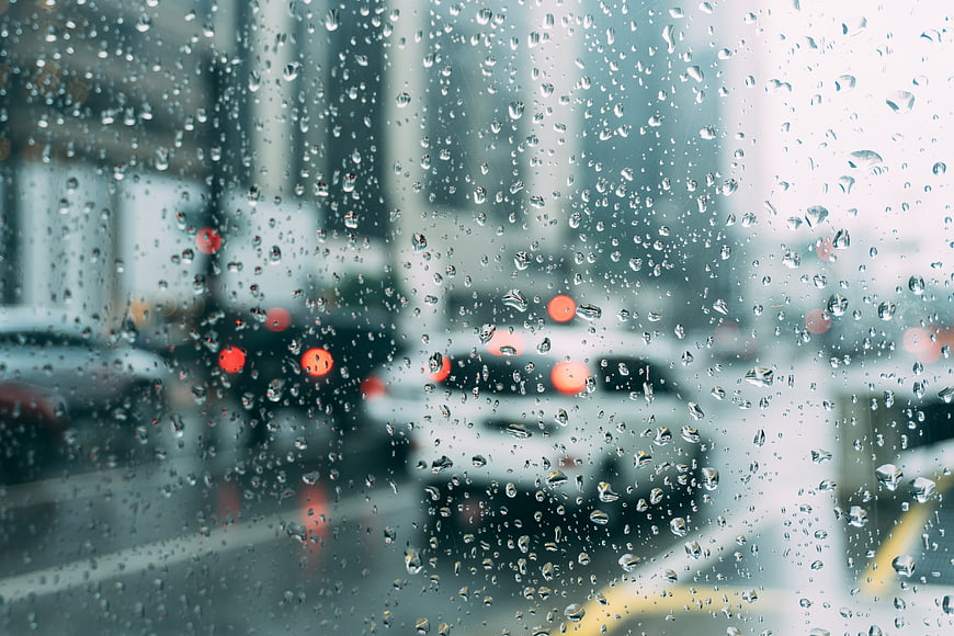 Raindrops on car windshield with blurred city traffic background