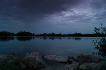 Dark moody lake landscape with rocks and cloudy sky at dusk