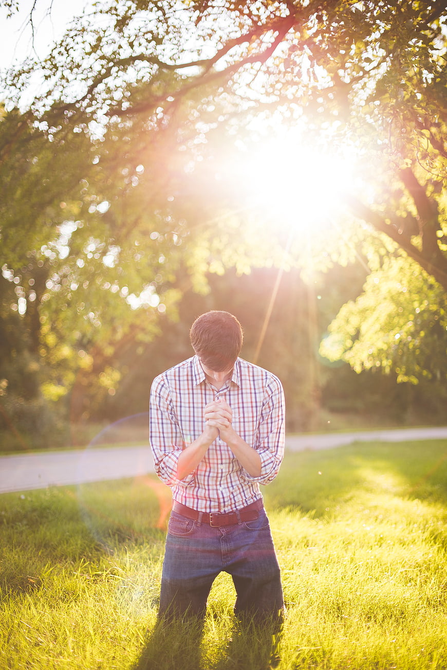 Man kneeling in prayer on grass with sun flare