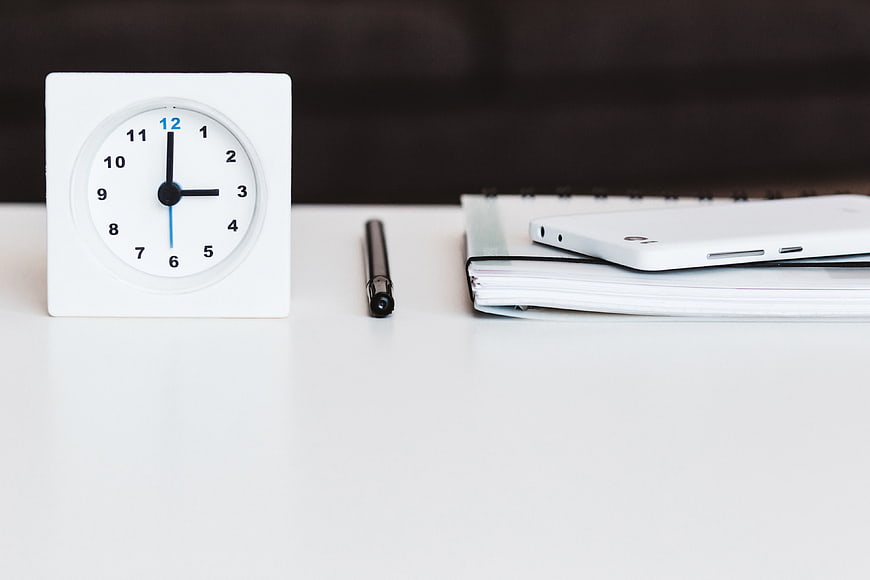 Minimalist white desk with clock, pen, notebook, and smartphone