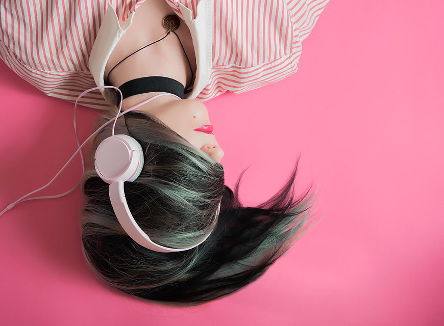 Woman with headphones lying on pink background