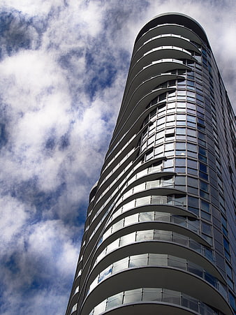 Low angle view of modern curved skyscraper against cloudy sky