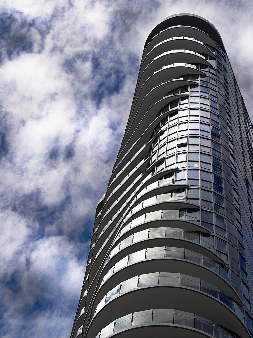 Low angle view of modern curved skyscraper against cloudy sky