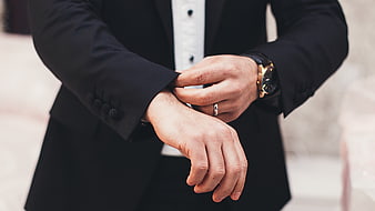Groom adjusting suit cuff with luxury watch and wedding ring
