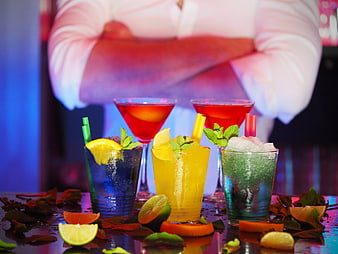 Colorful cocktails on a bar counter with bartender in background