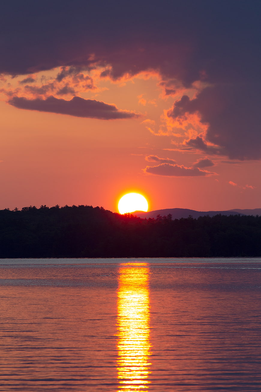 Vibrant sunset over lake with golden reflection and silhouetted trees