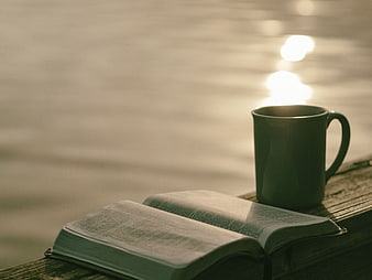 Open book and coffee mug on wooden dock by water