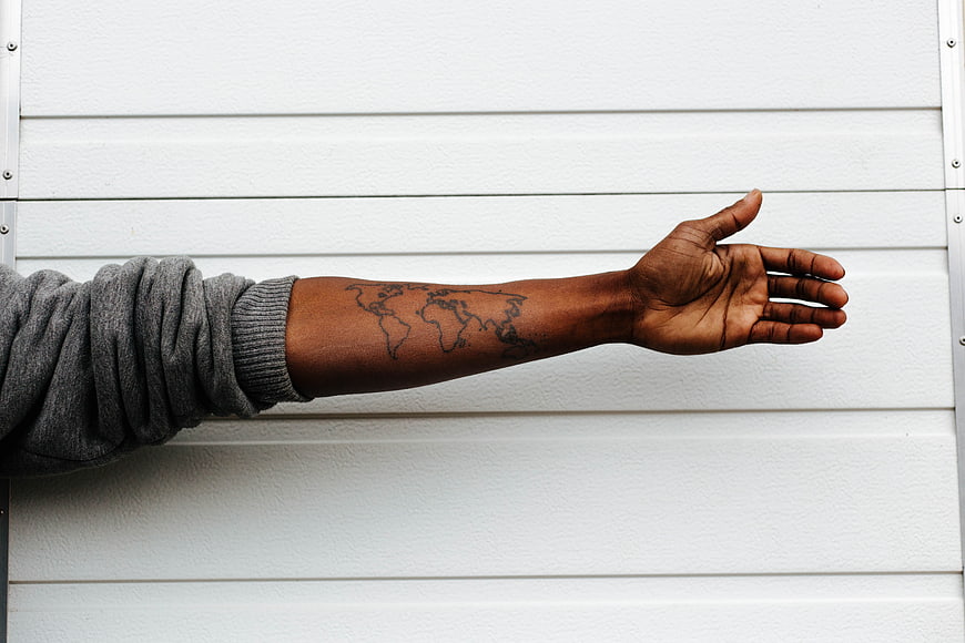 Man's arm with world map tattoo against white wall
