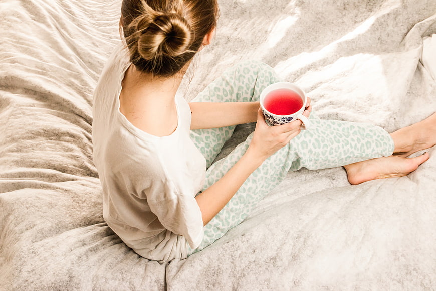 Woman in pajamas drinking tea in bed