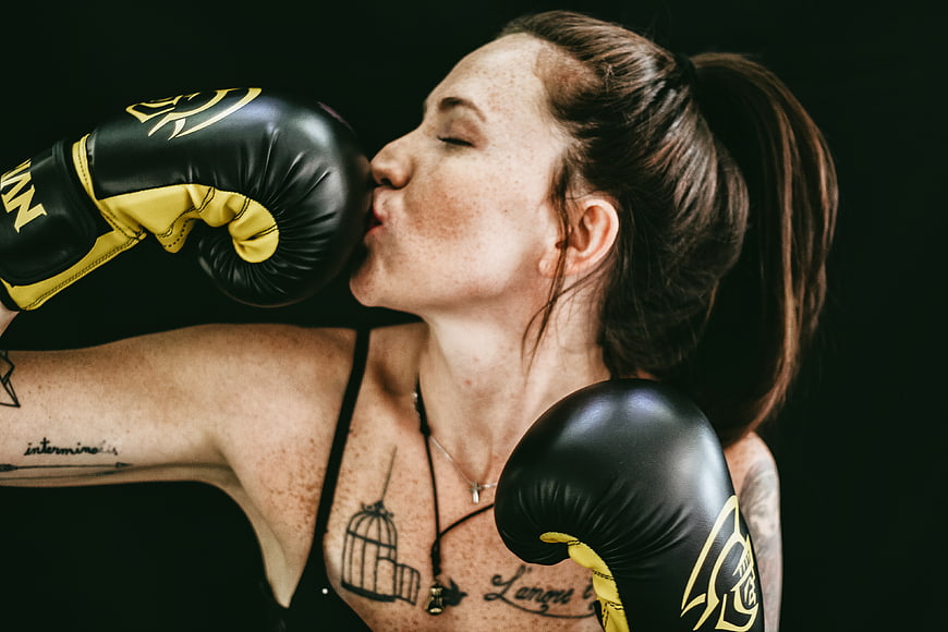 Woman kissing boxing glove in black and yellow gear