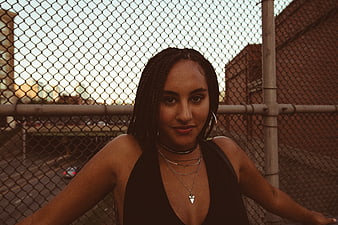 Portrait of stylish woman with braids leaning on chain link fence