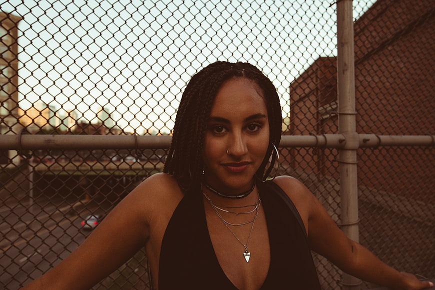 Portrait of stylish woman with braids leaning on chain link fence