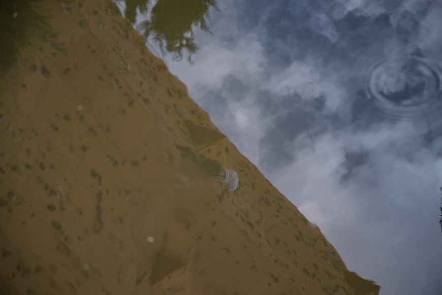 Reflection of rock climber on wet wall with sky and clouds