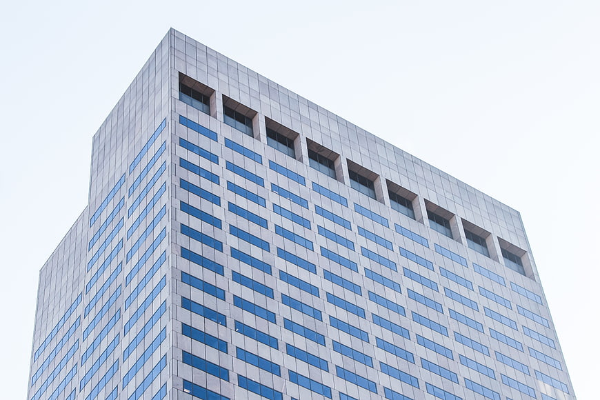 Low angle view of modern glass office building against white sky