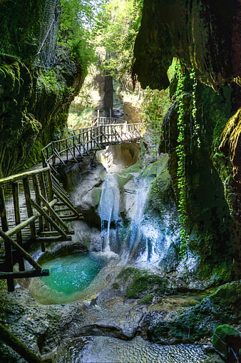 Lush tropical waterfall with wooden walkway in forest canyon