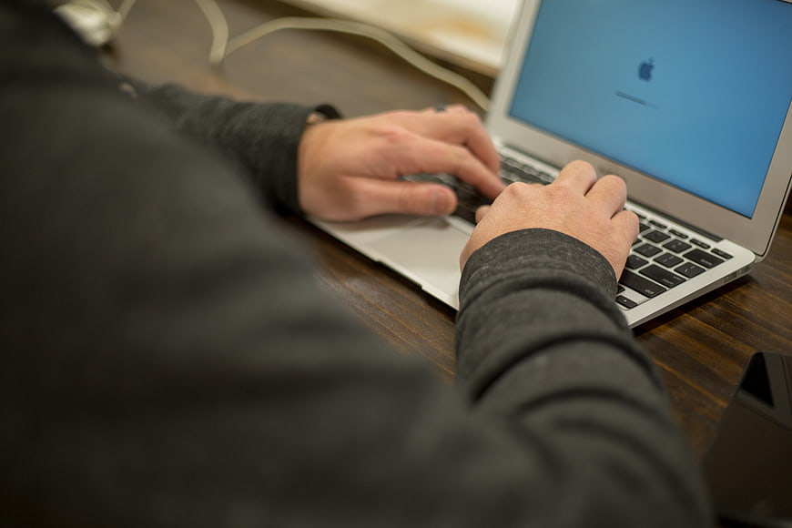 Close-up of hands typing on a laptop keyboard at a desk