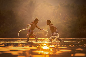 Two boys splashing water playfully in a river at sunset