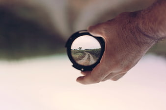 Hand holding camera lens with landscape reflection