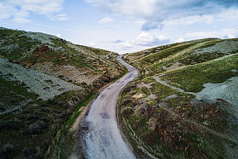 Winding dirt road through green rolling hills under cloudy sky