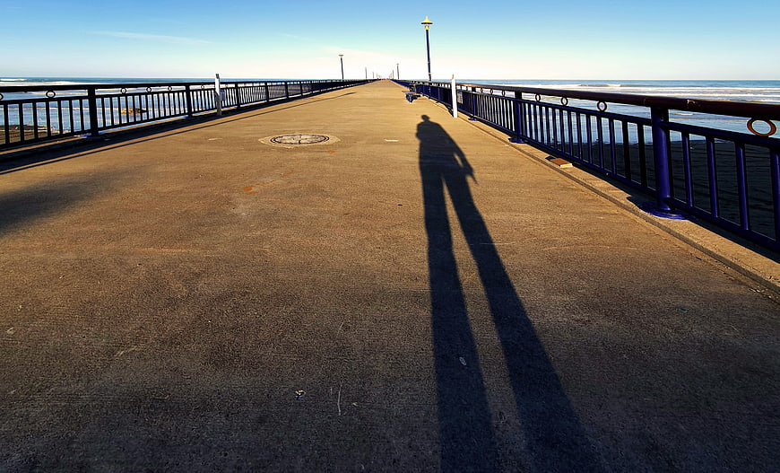 Long shadow of a person walking on a sunny pier