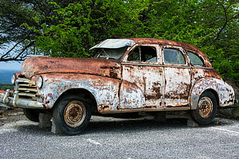 Rusty vintage car parked on pavement with green trees