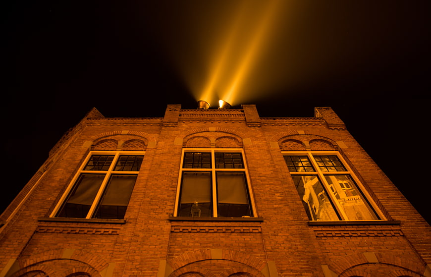 Brick building facade illuminated by searchlights at night
