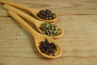 Wooden spoons with cloves, peppercorns, and dried herbs on wood