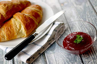 Golden croissants with red jam on rustic wooden table