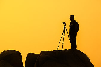 Silhouette of photographer with camera on tripod at sunset