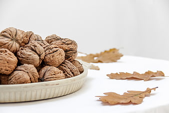 Walnuts in ceramic bowl with autumn oak leaves on white background