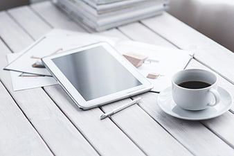 White tablet, stylus, and coffee on wooden table