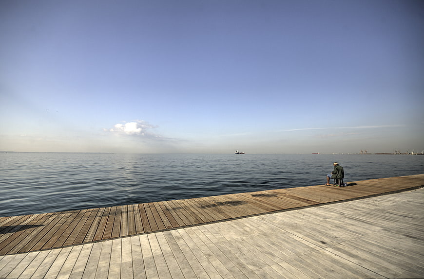 Man fishing alone on wooden pier by calm sea