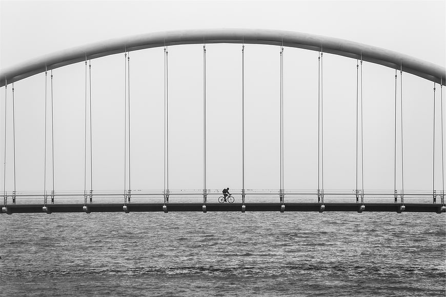 Cyclist on modern arched bridge over water in black and white