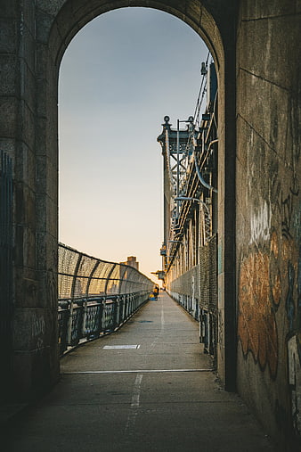Man walking on bridge path through stone archway at sunset