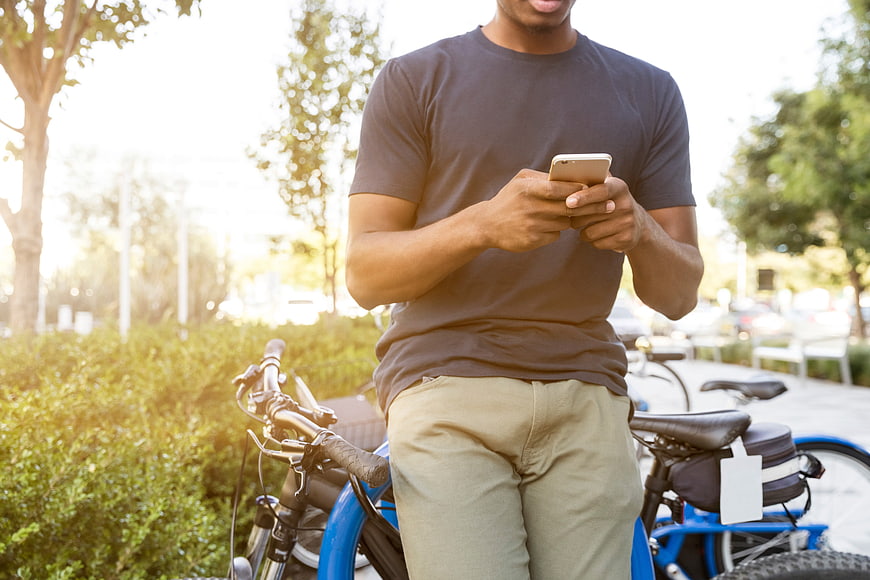 Man using smartphone next to blue bicycle outdoors