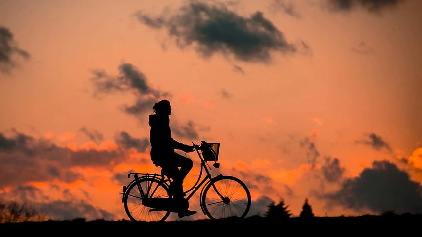 Silhouette of Cyclist Riding Bike Against Orange Sunset Sky
