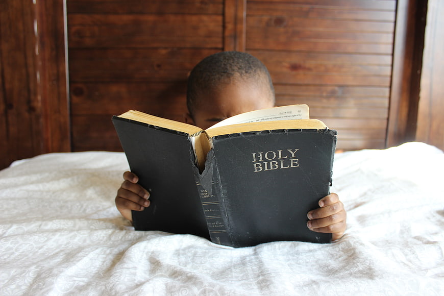 Child Reading Holy Bible in Bed