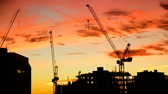 Silhouette of Construction Cranes Against Vibrant Sunset Sky
