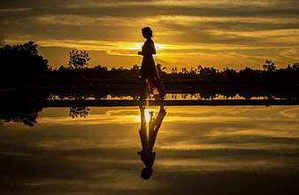 Silhouette of woman walking by water at golden sunset