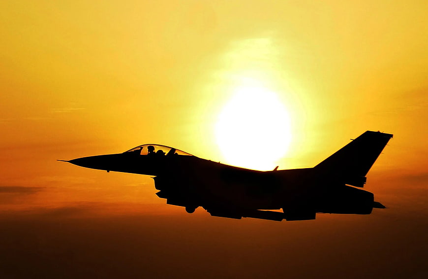 Silhouette of fighter jet flying against golden sunset sky