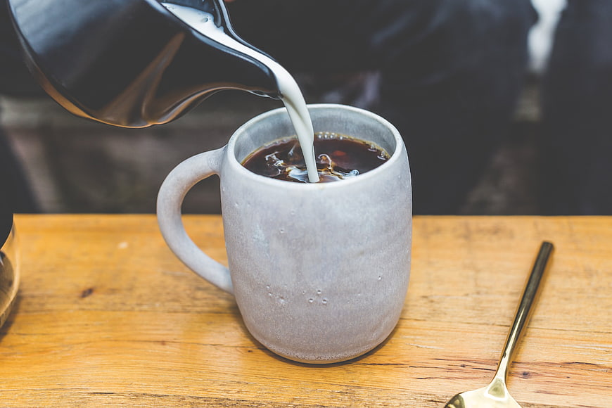 Pouring milk into coffee cup on wooden table