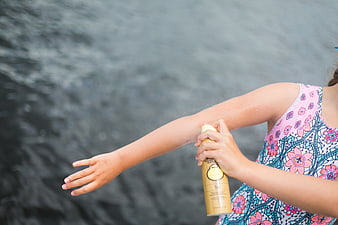Girl applying sunscreen spray at the lake