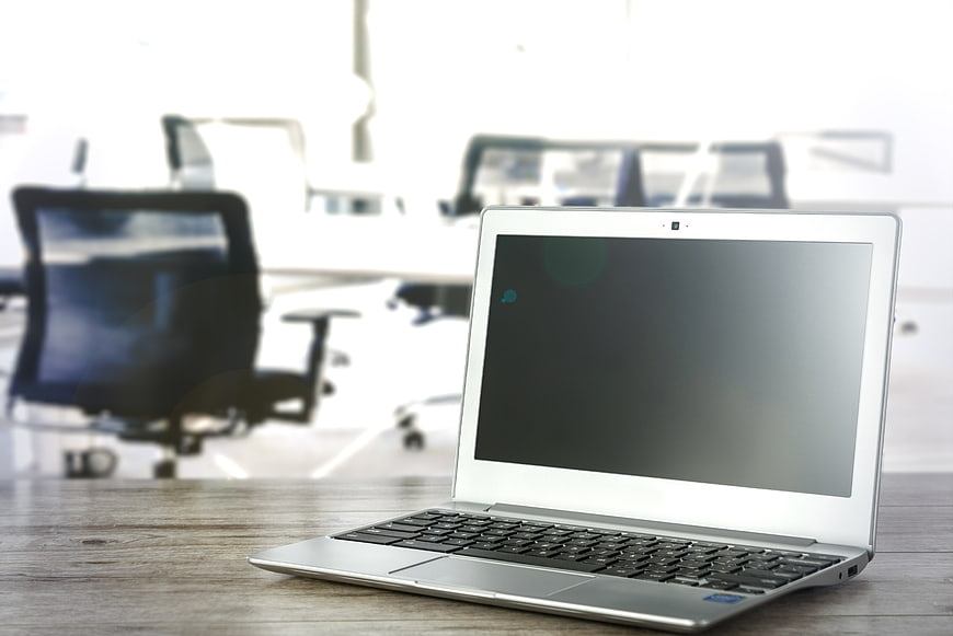 Silver laptop on wooden desk in blurred office background