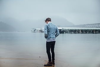 Man in Denim Jacket Standing on Foggy Beach Shore