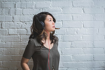 Woman with headphones listening to music against white brick wall