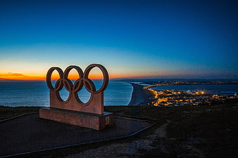Olympic Rings Sculpture at Sunset Over Coastal City