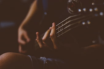 Close-up of hands playing electric bass guitar in dim light