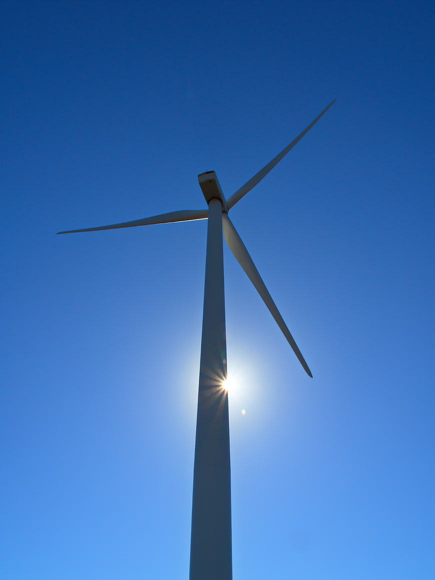 Low angle view of wind turbine against blue sky with sun flare