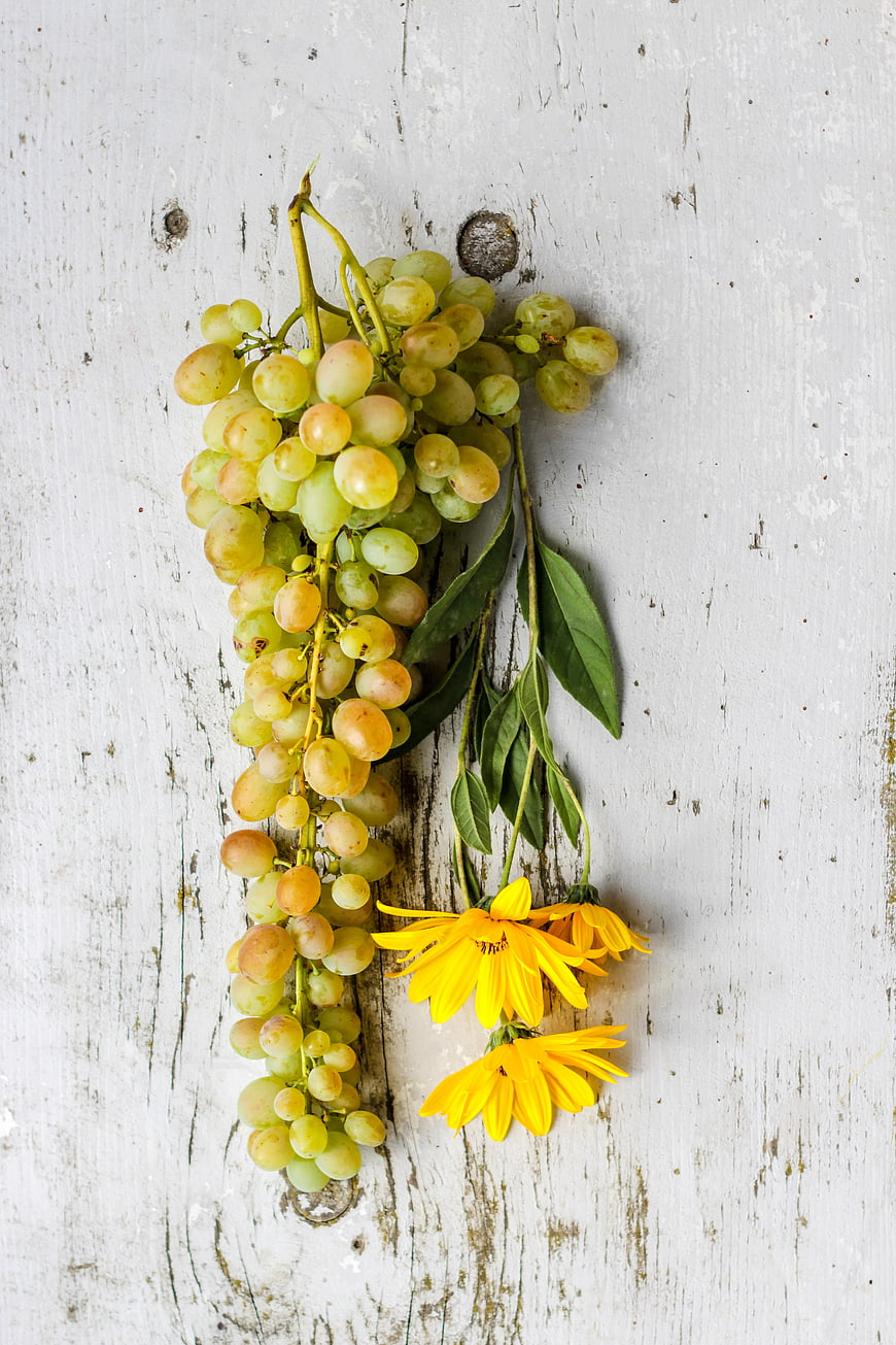 Flat lay of green grapes and yellow flowers on rustic wood