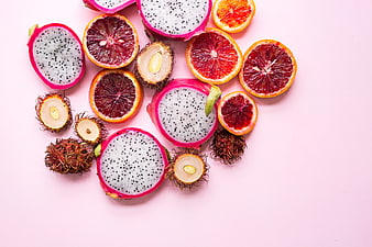 Flat lay of sliced dragon fruit, blood orange, and rambutan on pink background